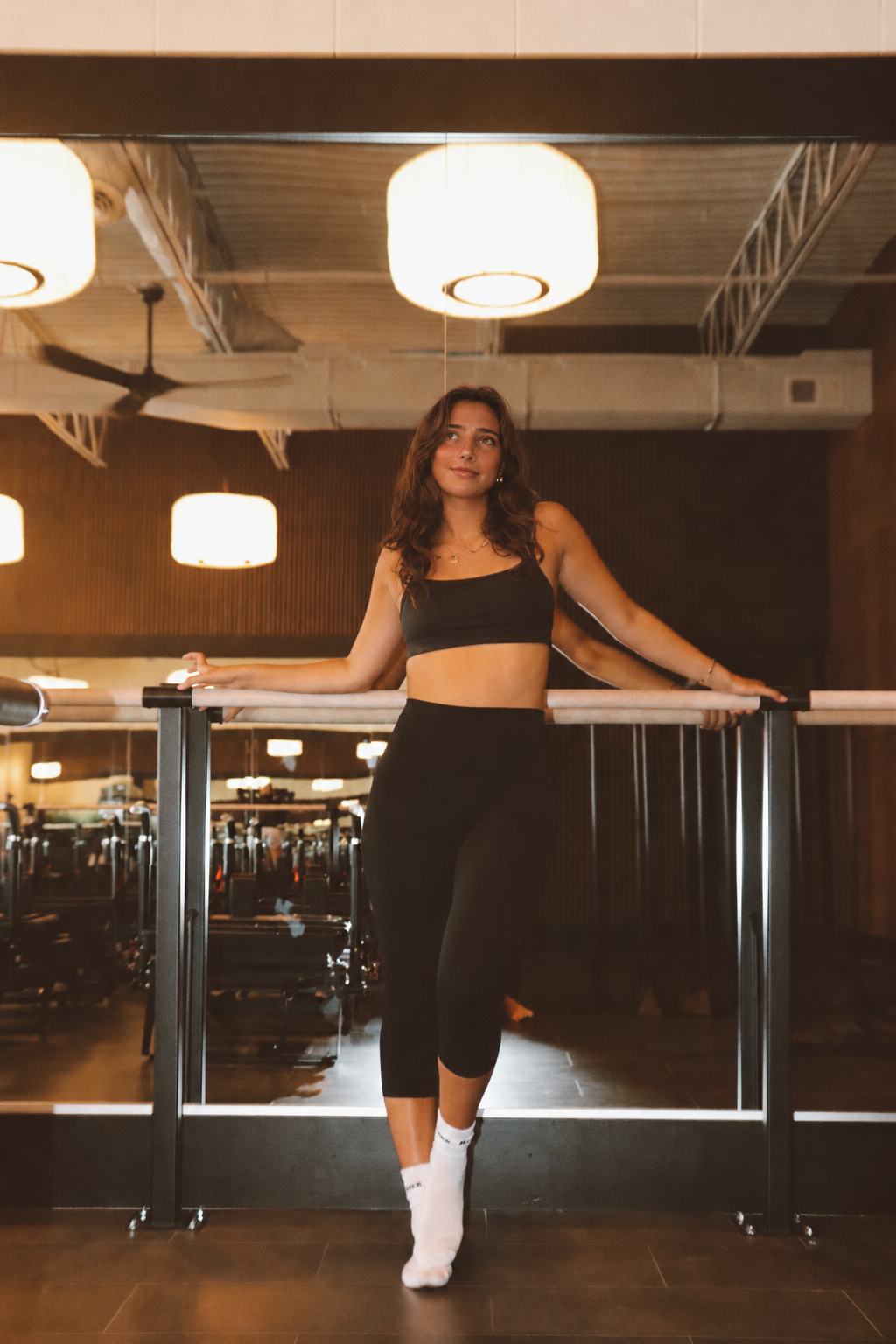 Sam, founder of flowhouse, in a warm-toned editorial portrait holding hand weights overhead.